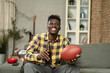 © JustLife - Young African man watching sport match on television and supporting his favorite team. Happy man enjoying victory, watching sports competition on tv..