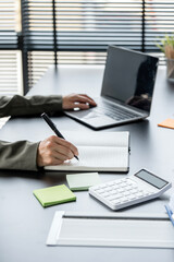 Wall Mural - Businesswoman hand writing note or business plan and working on laptop computer at her desk in modern office.