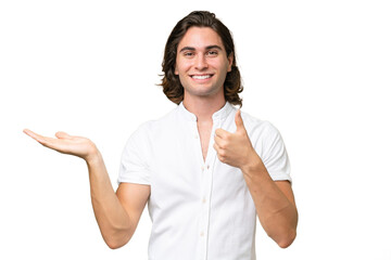 Wall Mural - Young caucasian man isolated on green chroma background holding copyspace imaginary on the palm to insert an ad and with thumbs up