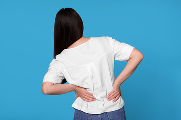 Sticker - Young woman suffering from pain in back on light blue background. Arthritis symptoms