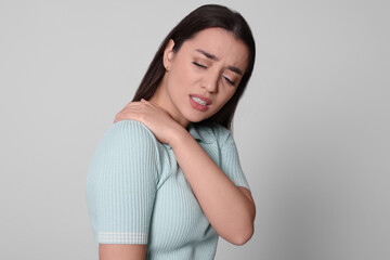 Canvas Print - Young woman suffering from pain in shoulder on light grey background. Arthritis symptoms