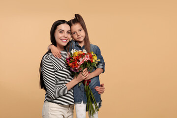 Poster - Happy woman with her cute daughter and bouquet of beautiful flowers on beige background, space for text. Mother's day celebration