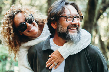 Wall Mural - Youthful mature people enjoying weekend activity together. Man carrying woman in piggyback and having fun with love. Man wearing glasses and woman hugging him. Happy life and relationship. Together