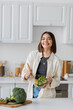 © LIGHTFIELD STUDIOS - Positive woman mixing fresh and vegetarian salad in kitchen.