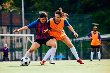 Female players tackling during soccer practice on playing field.