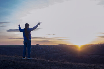 Wall Mural - A girl with raised hands on the background of the sky. Prayer. Glorification of God. Worshiping Jesus