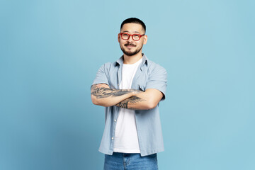 Smiling Asian man wearing stylish red eyeglasses and casual clothes isolated on blue background