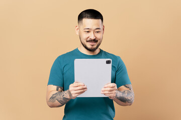 Wall Mural - Smiling asian man using digital tablet isolated on beige background. Successful businessman online shopping