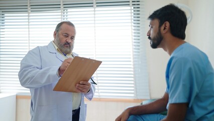 Wall Mural - Caucasian senior male doctor consulting and writing a prescription to Indian male patient. Healthcare and medically concept