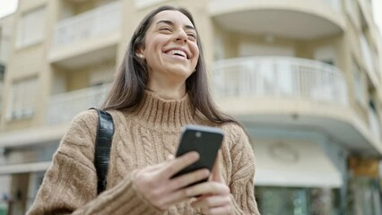 Wall Mural - Young beautiful hispanic woman using smartphone smiling at street