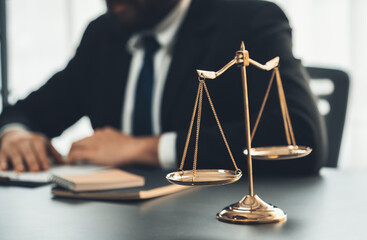 Wall Mural - Focus shiny golden balanced scale on blurred background of lawyer working in his desk at law firm office. Scale balance for righteous and equality judgment by lawmaker and attorney. Equilibrium