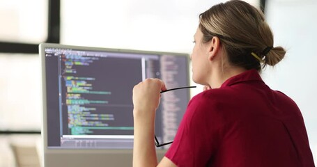 Female programmer with glasses in hand checkups code working on computer in office. Software developer sits at workplace slow motion