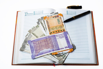 Wall Mural - pile of indian money with pen over open notebook on a white background. Save money concept.