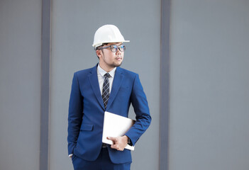 Handsome engineer wearing suit and hard hat or white helmet on building background. Engineer using tablet for checking construction about modern building. copy space for text.