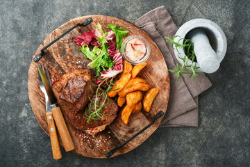 Steaks. Sliced grilled meat steak New York, Ribeye or Chuck roll with with garnished with salad and french fries on black marble board on old wooden background. Top view. Mock up.