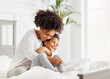 © JenkoAtaman - Happy ethnic family. African american mother and daughter play and laugh in bed.