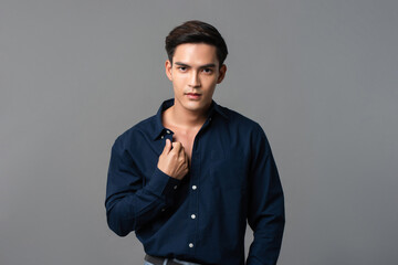 Wall Mural - Studio portrait of young handsome Asian man wearing dark blue shirt looking at camera in light gray isolated background