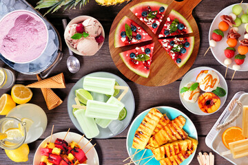 Poster - Refreshing summer food table scene. Assorted grilled fruits, ice cream and ice pops. Above view on a dark wood background.