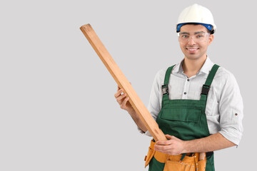 Poster - Young carpenter with wooden plank on grey background