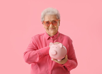 Senior woman with piggy bank on pink background