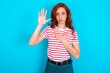 young redhead woman wearing striped T-shirt over blue background Swearing with hand on chest and open palm, making a loyalty promise oath