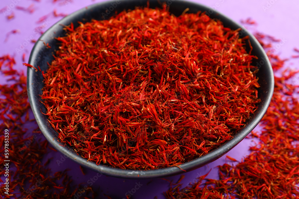 Bowl with pile of saffron on purple background