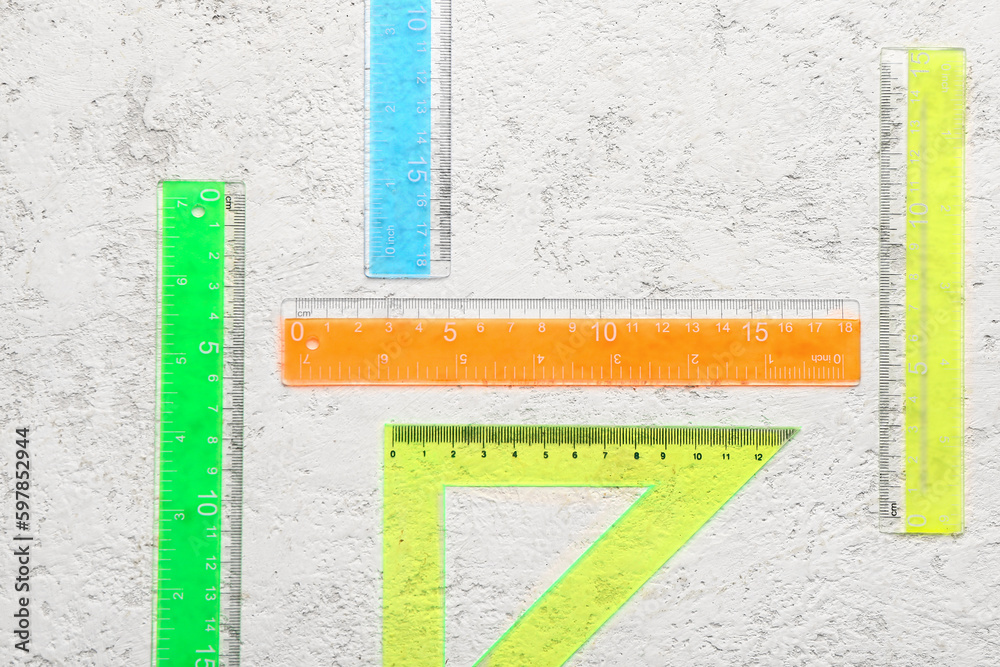 Colorful straight and triangle plastic rulers on light grunge background