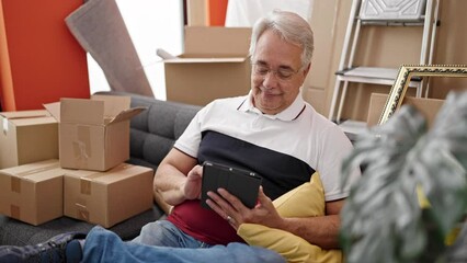 Poster - Middle age man with grey hair sitting on the sofa using tablet at new home