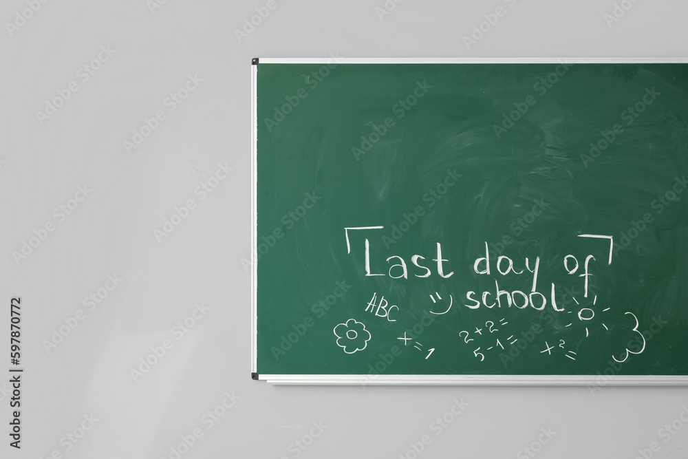 Blackboard with text LAST DAY OF SCHOOL and drawings on white wall