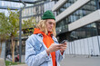 Millennial hipster guy with blond hair browsing internet on mobile phone, standing on city street, stylish young man messaging online while waiting or friends outdoors. Urban lifestyle and smartphone
