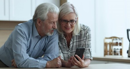 Wall Mural - Attractive senior couple spend leisure on internet, look at cell phone screen watching videos, enjoy new mobile apps, surfing social media, scroll news feed. Older generation use modern Generative AI