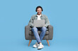 © New Africa - Happy man with laptop and headphones sitting in armchair on light blue background