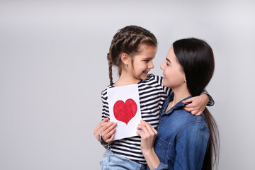 Poster - Happy woman with her daughter and handmade greeting card on light grey background, space for text. Mother's day celebration