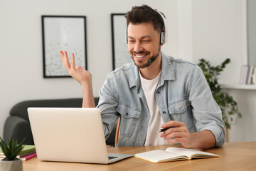 Wall Mural - Man in headphones studying on laptop at home. Online translation course