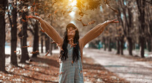 Beautiful Young Woman Throwing Autumn Yellow Leaves. Portrait Of Joyful Woman Playing With Leaves In Park During Fall.