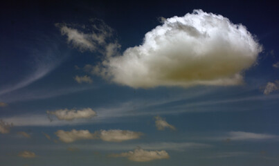 A fluffy cloud with wispy clouds against blue sky. 