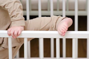 Baby escapes from the crib by climbing over the bars. The child climbs over the railing bed. Kid aged about two years (one year nine months)