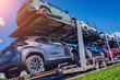 Car carrier trailer transports cars on highway at blue sky background. 