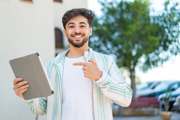 Wall Mural - Handsome Arab man holding a tablet at outdoors and pointing it