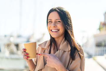 Wall Mural - Young woman at outdoors holding a take away coffee with happy expression