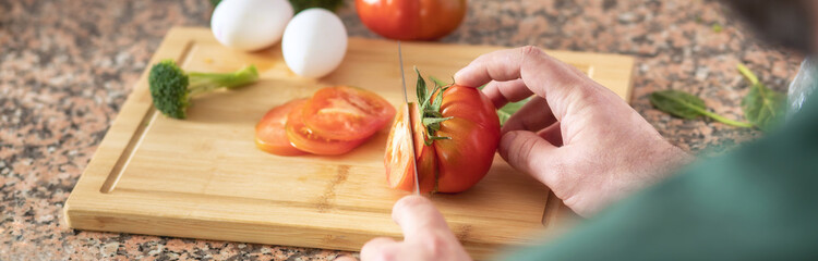 Canvas Print - Man cooking delicious and healthy food breakfast at home kitchen. Close up of male hands cuts a tomato on a cutting board