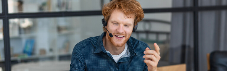 Smiling man call center worker in headphones is working at modern office. Portrait of a happy male support employee, smiles