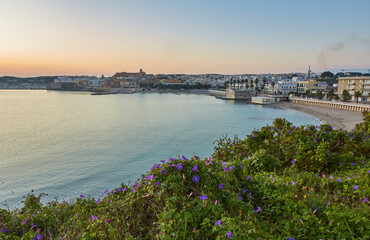 Wall Mural - beautiful orange sunset or sunrise over the harbor of Otranto, Italy. Soft clouds, calm ocean and backlit skyline and marina with yachts and fishermen.