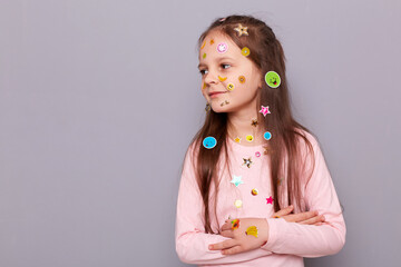 Wall Mural - Optmistic smiling little girl covered colorful kid's stickers standing isolated over gray background lookign away and advertisement area, copy space for promotion.