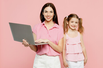 Wall Mural - Happy smiling IT woman wear casual clothes with child kid girl 6-7 years old. Mother daughter hold use work on laptop pc computer isolated on plain pastel pink background. Family parent day concept.