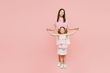 Wall Mural - Full body smiling happy fun woman wear casual clothes with child kid girl 6-7 years old. Mother stand behind daughter, hold hands isolated on plain pastel pink background. Family parent day concept.