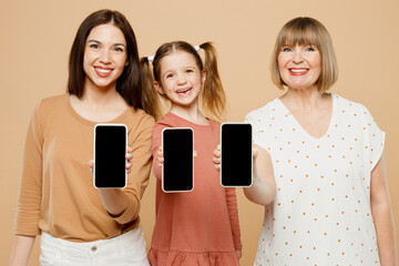 Wall Mural - Happy women wearing casual clothes with child kid girl 6-7 years old. Granny mother daughter hold use blank screen area mobile cell phone isolated on plain beige background. Family parent day concept.