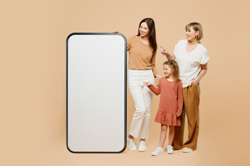Wall Mural - Full body women wear casual clothes with child kid girl 6-7 years old. Granny mother daughter near big huge screen area mobile cell phone isolated on plain beige background. Family parent day concept.