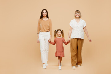 Poster - Full body smiling fun cheerful women wearing casual clothes with child kid girl 6-7 years old. Granny mother daughter walk holding hands isolated on plain beige background. Family parent day concept.