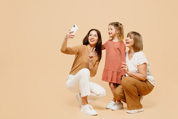 Wall Mural - Full body women wear casual clothes with child kid girl 6-7 years old. Granny mother daughter do selfie shot mobile cell phone show v-sign isolated on plain beige background Family parent day concept